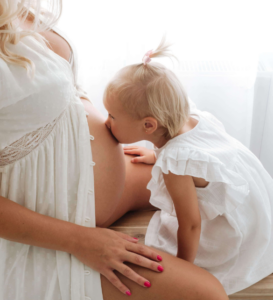 Baby kissing their pregnant mum's baby bump during a maternity photography session in Surrey.